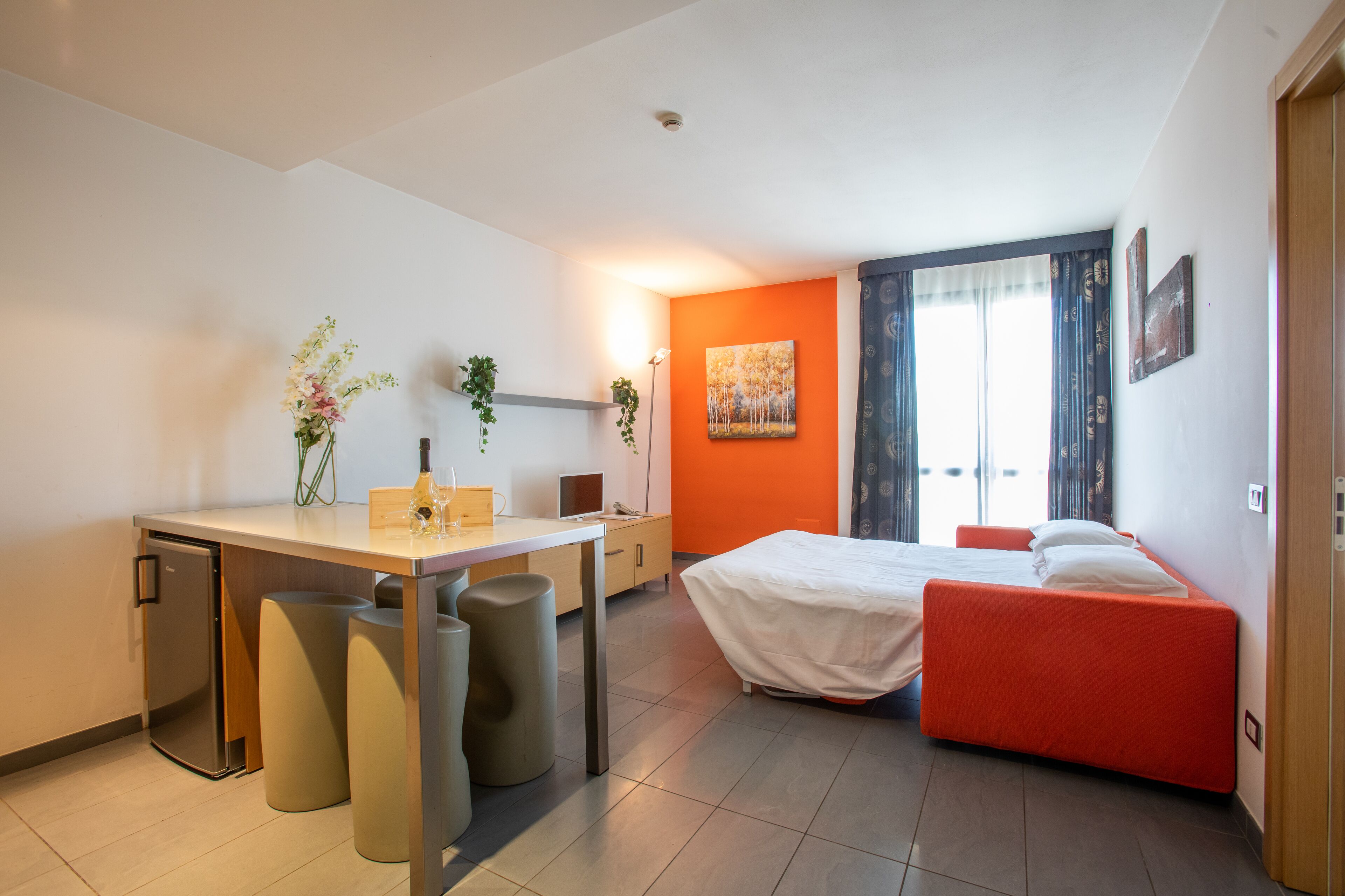 Ein kleines Hotelzimmer mit Bett, Schreibtisch und einer kleinen Küchenzeile.