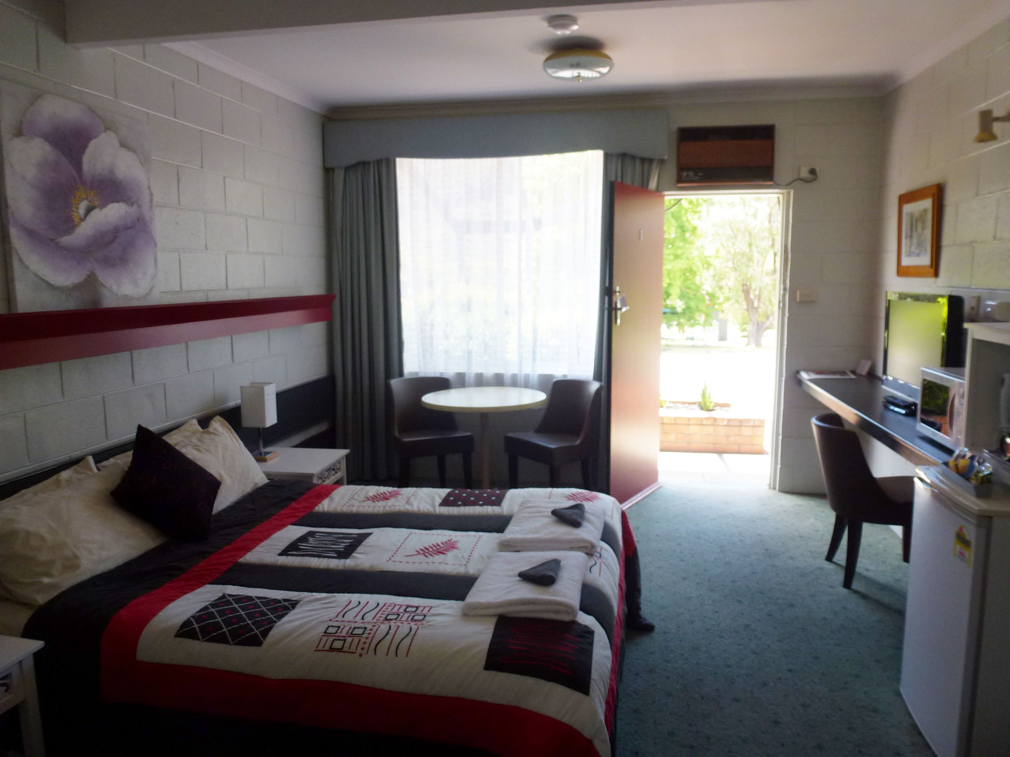 A hotel room with a bed, a desk, a chair, a table, and a window with curtains.