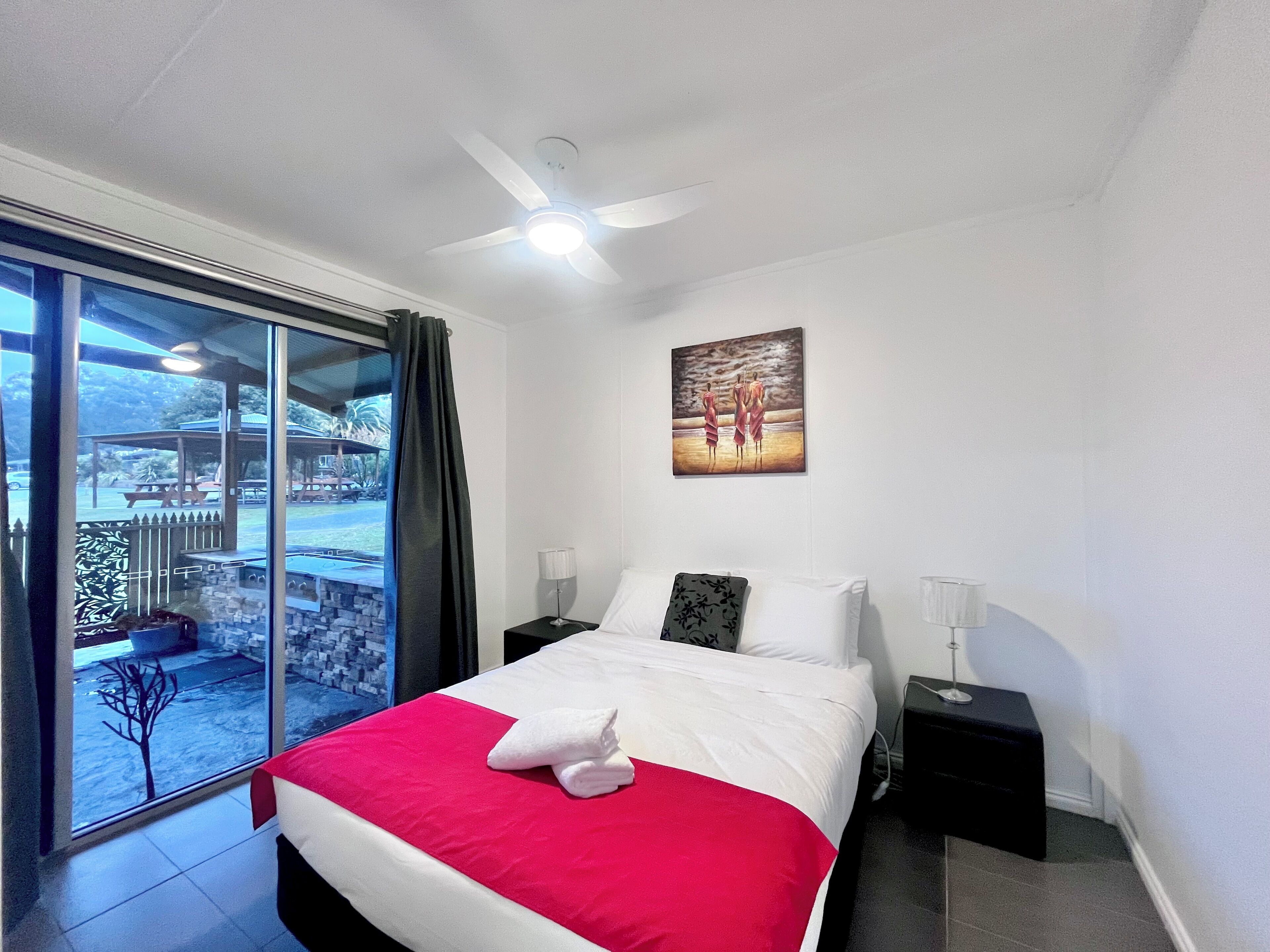 Ein Hotelzimmer mit Bett, einem Gemälde, einem Deckenventilator, einem Nachttisch und Blick ins Freie.