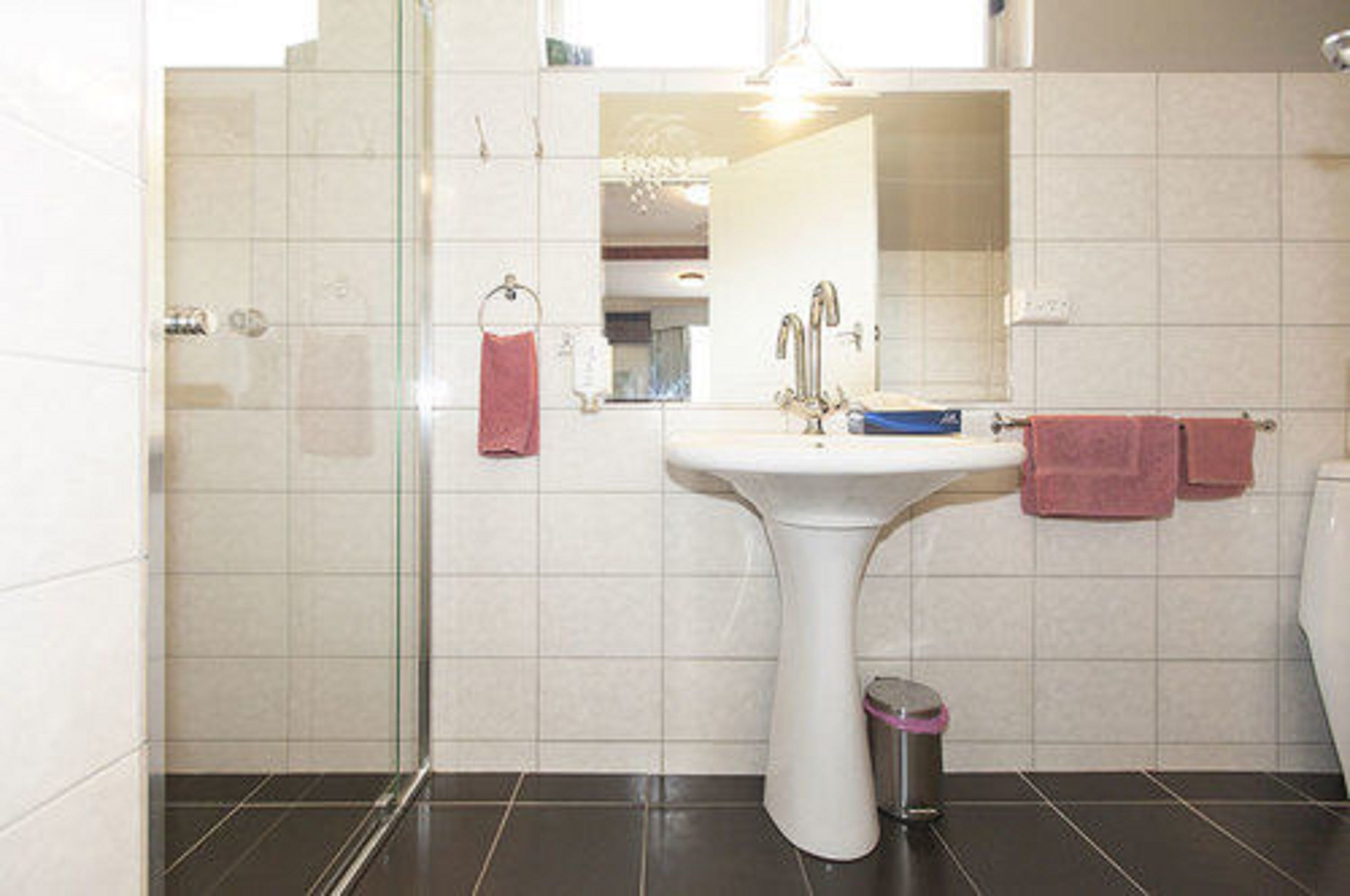 Um banheiro moderno com box de vidro, pia de pedestal e vaso sanitário.