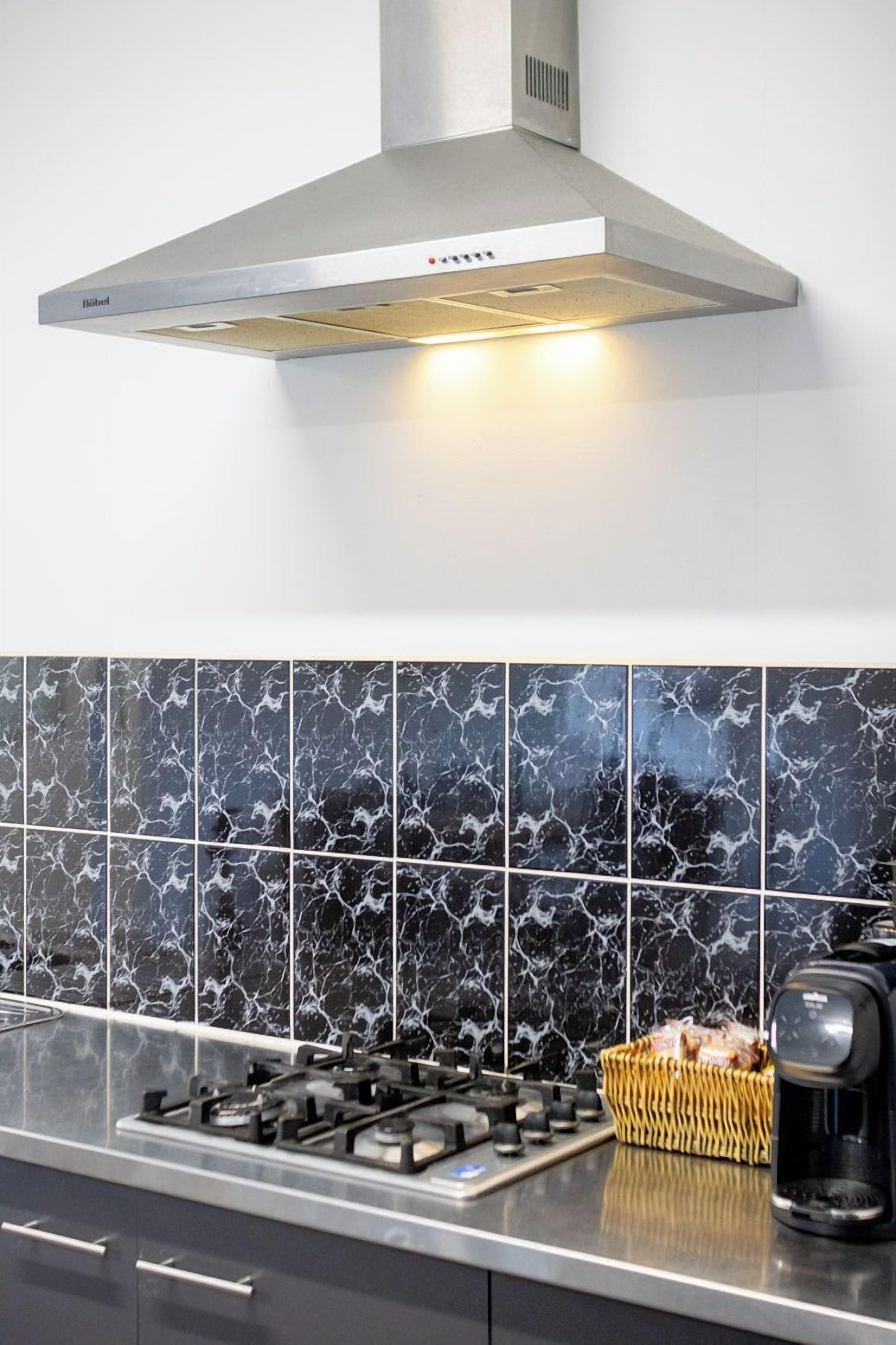 Una cocina con estufa a gas, extractor de acero inoxidable y cafetera sobre la encimera.