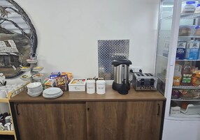Una barra de desayuno con platos apilados, café, azúcar y recipientes para té. Hay una cafetera y un tostador sobre la encimera.