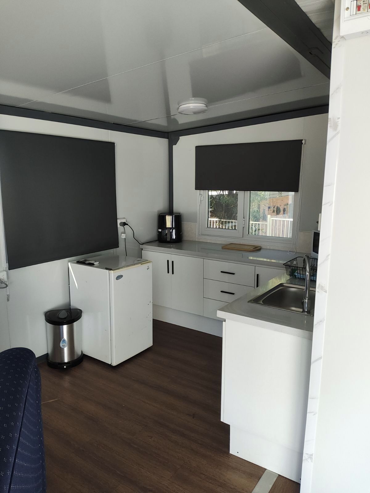 A compact kitchen with white cabinets, a small refrigerator, a coffee maker, and a sink.