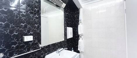 A modern bathroom with a black marble wall, a white sink, a mirror, a towel dispenser, and a shower area.