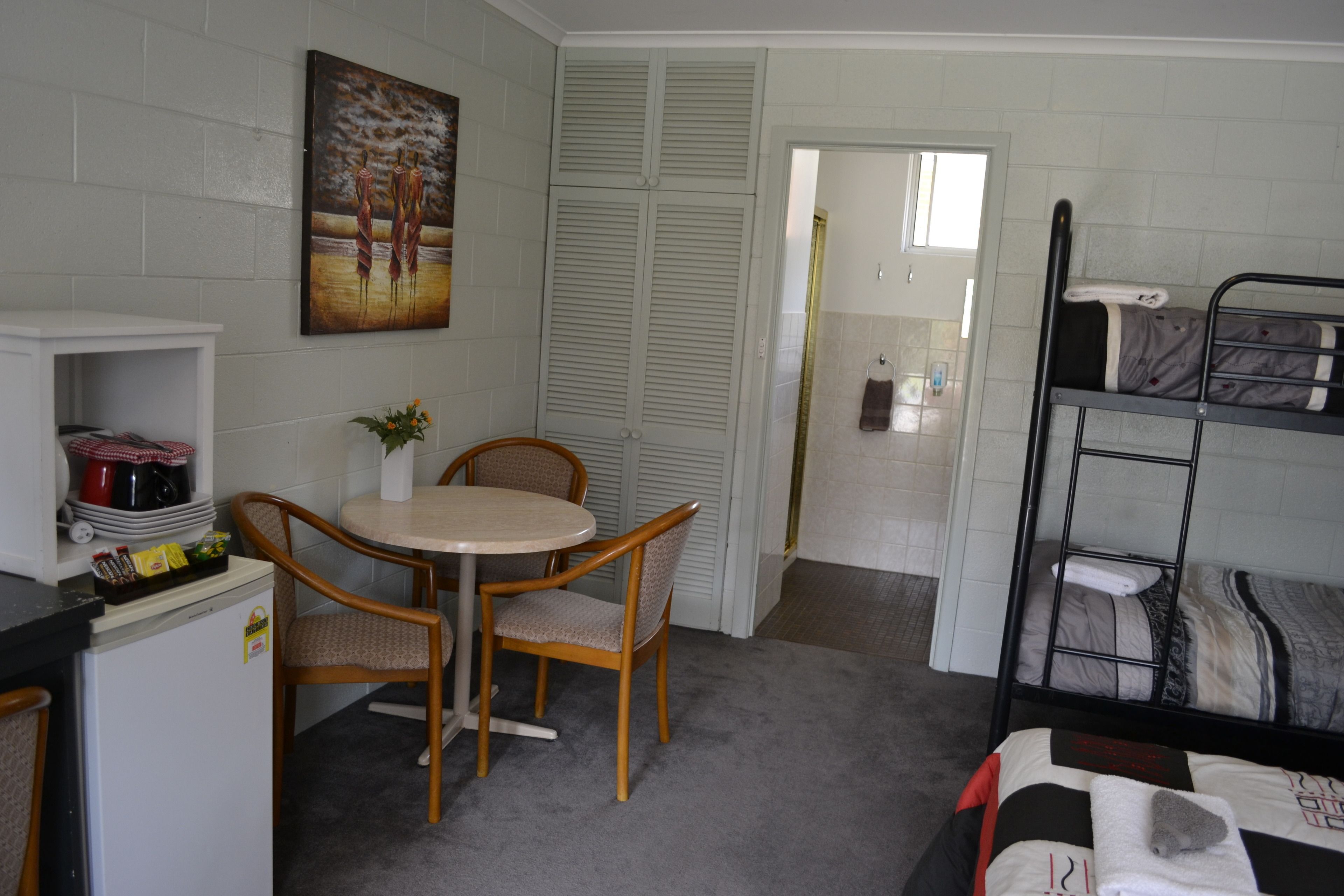 A compact room with a bunk bed, a small kitchenette, a dining table with chairs, and a painting on the wall.