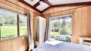 A bedroom with a large bed, wooden walls, and a view of a green landscape.
