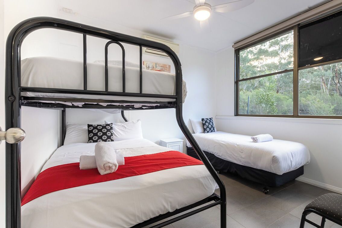 Una habitación con una litera, una cama individual y un ventanal con vistas a árboles.