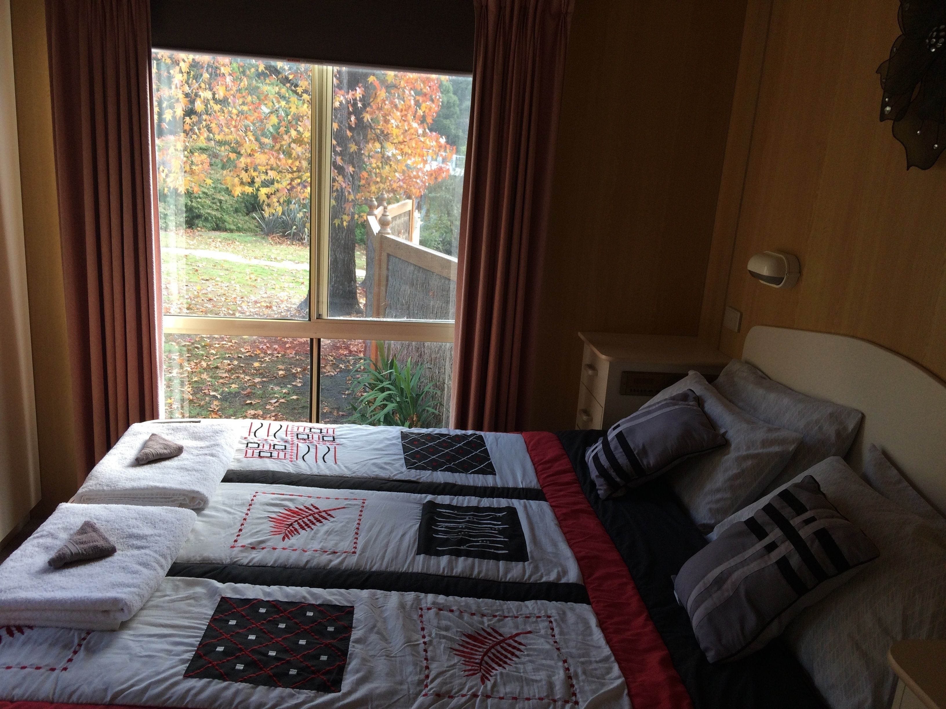 A bedroom with a large window, a bed with multiple pillows and a quilt, and a nightstand with a lamp.