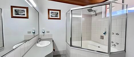 A modern bathroom with a white sink, a glass-enclosed shower, and wooden ceiling accents.