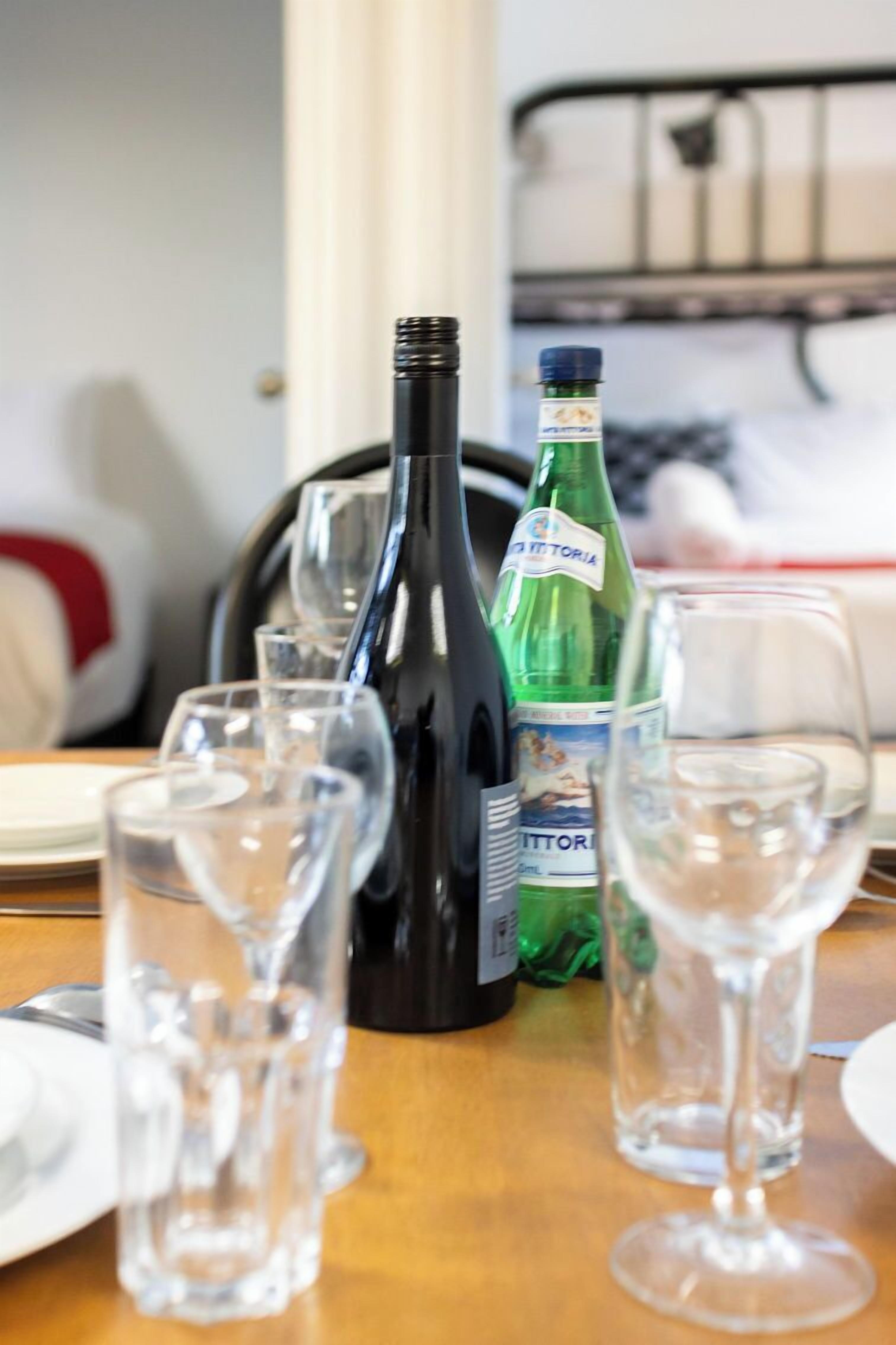 Una mesa con una botella de agua, una botella de líquido verde y varios vasos de vino.