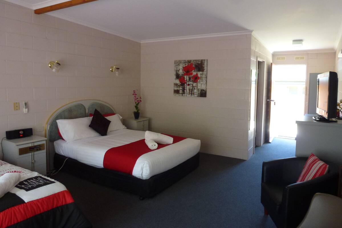 Et hotelværelse med seng, natbord, fjernsyn og en stol.