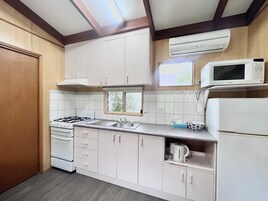 Una cocina compacta con armarios blancos, estufa a gas, microondas y refrigerador.