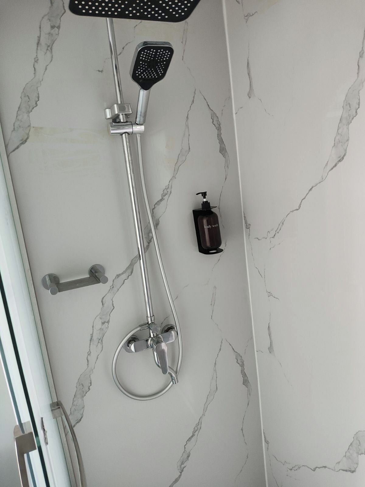 A shower with a handheld showerhead, a wall-mounted faucet, and a handheld soap dispenser.