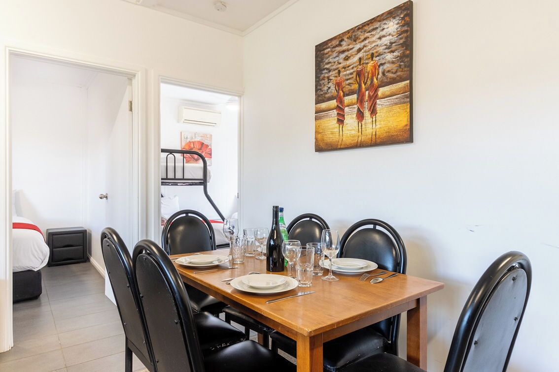 Un coin repas avec une table en bois dressée pour quatre personnes, des chaises noires et un tableau accroché au mur.