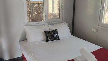 A neatly made bed with white and red bedding, a decorative pillow, and a rolled towel on the bed.