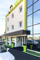 Un edificio moderno con una amplia fachada de vidrio, un letrero llamativo sobre la entrada y un estacionamiento al frente.