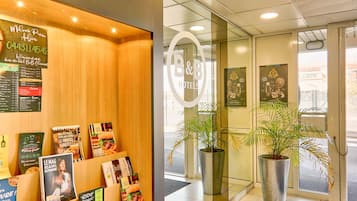 A hotel reception area with a wooden reception desk, a glass door entrance, and potted plants.
