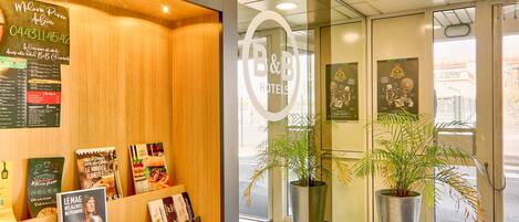 A hotel reception area with a wooden reception desk, a glass door entrance, and potted plants.