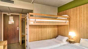 Une chambre avec un lit superposé doté d’une tête de lit en bois, une table de chevet avec une lampe et une porte avec une pancarte.