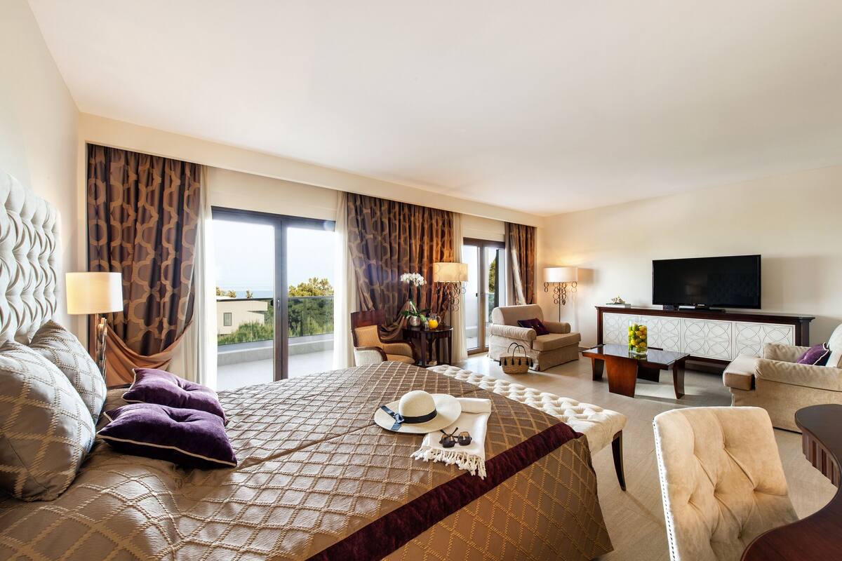 A hotel room with a large bed, a sofa, a TV, and a dining area.