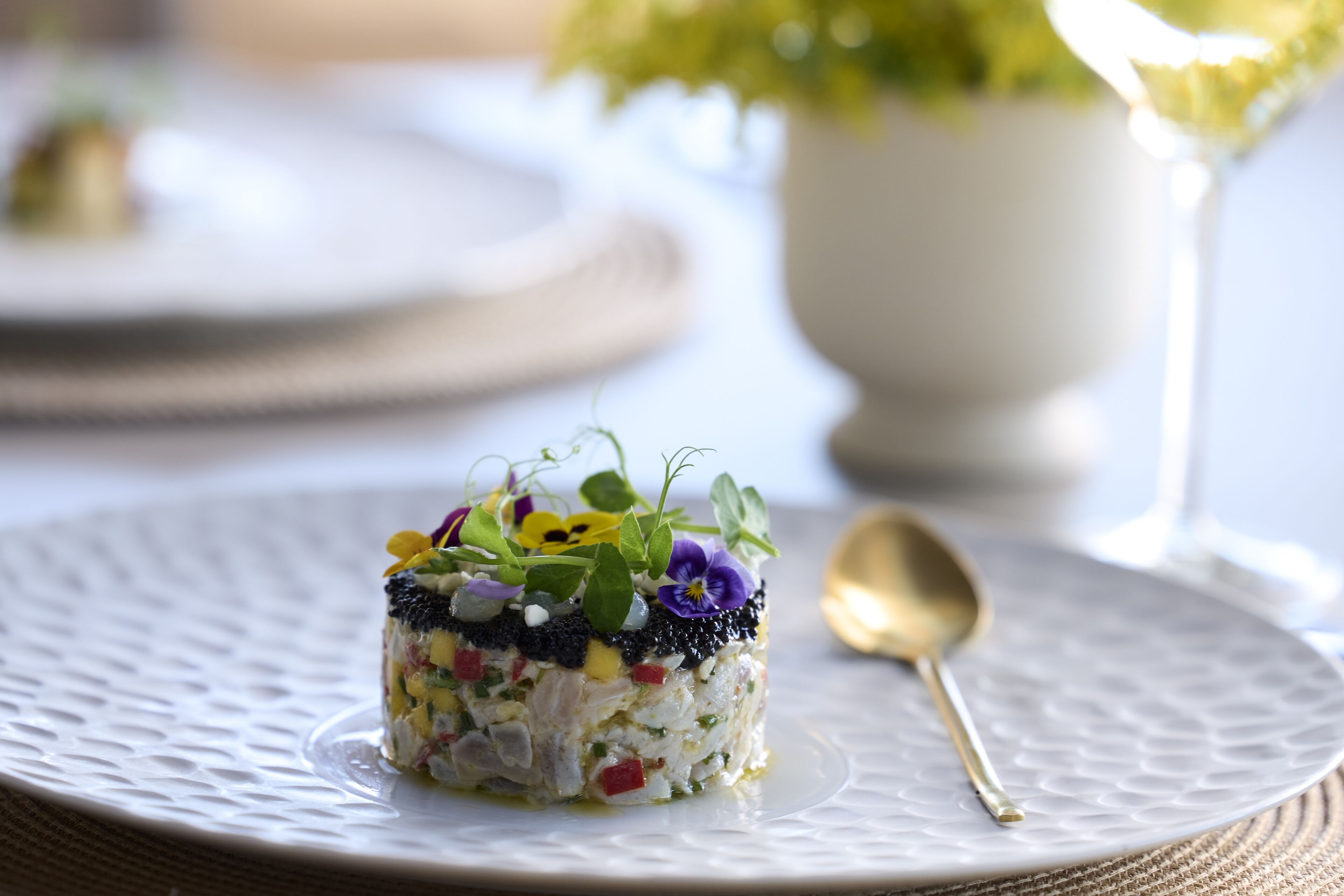 A plated dish with a variety of ingredients, a gold spoon, and a white textured plate.