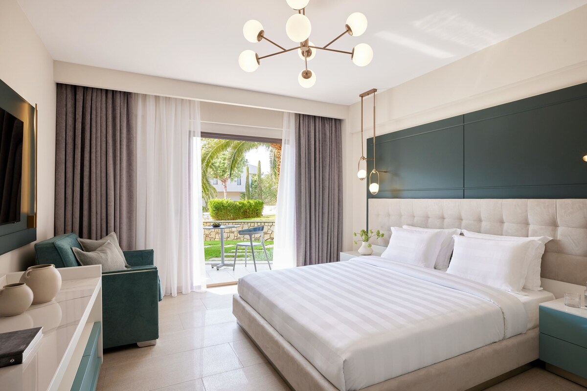 A modern hotel room with a large bed, a desk, and a view of the outdoors.