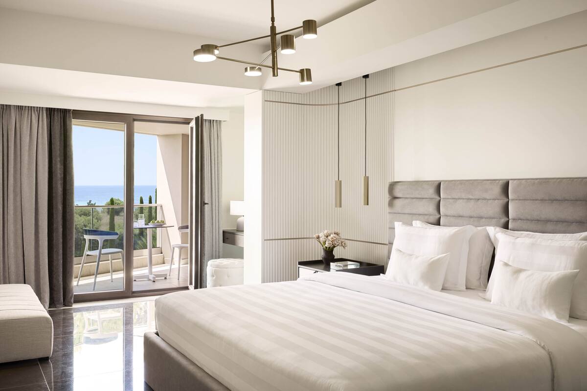 A modern hotel room with a large bed, a balcony with a view, and a stylish ceiling light fixture.