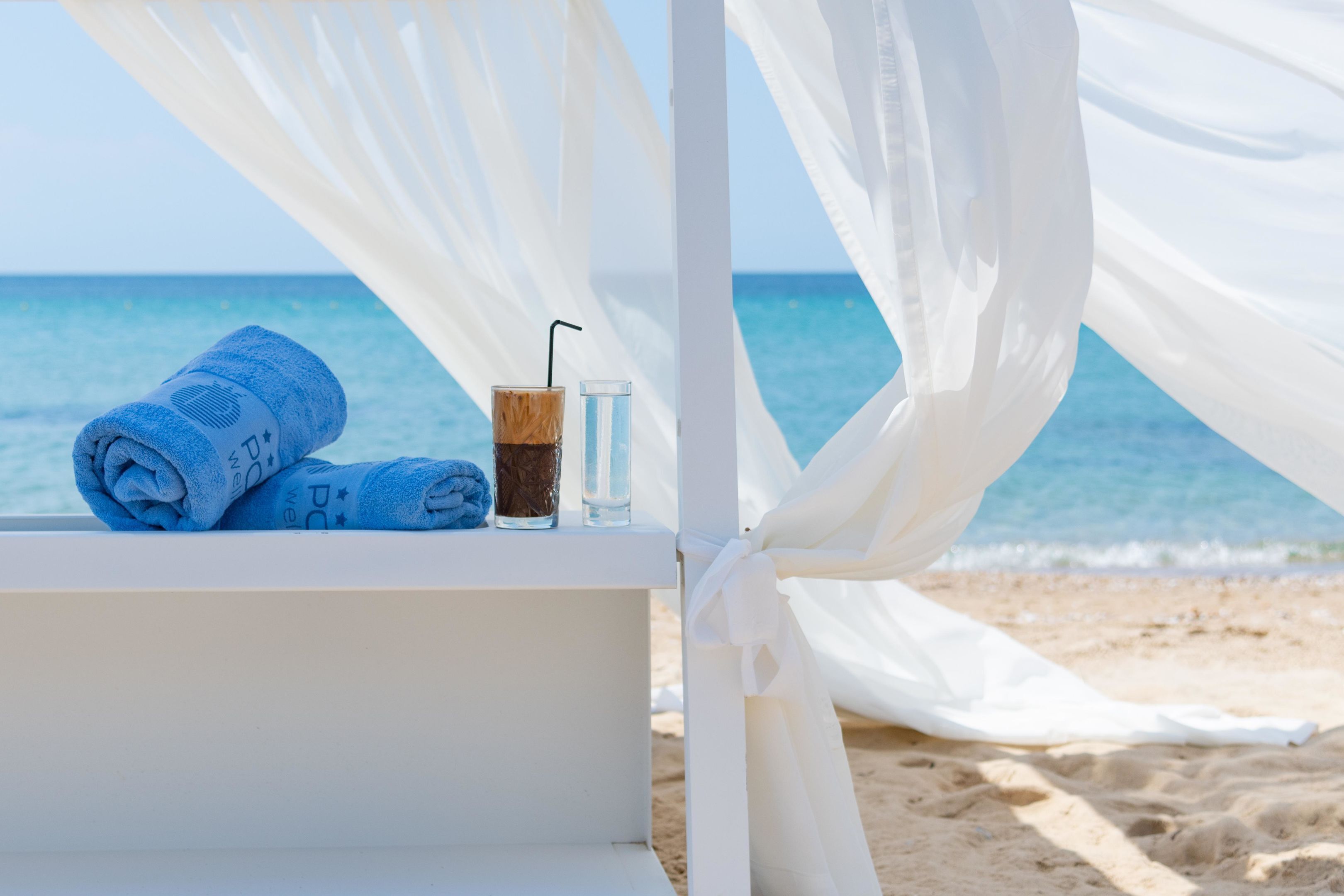A beach setting with a white canopy, a bathtub, and a glass of iced coffee.