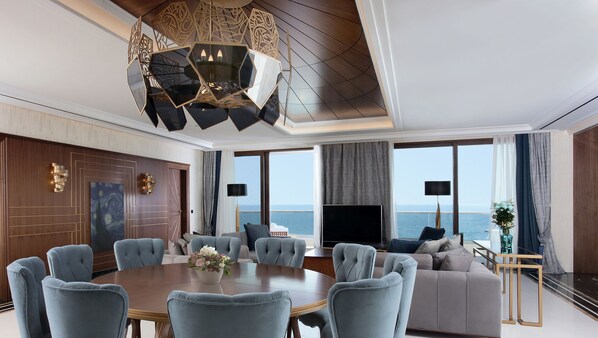 A spacious living area with a large round table, comfortable seating, a modern chandelier, and a view of the sea through large windows. - Pomegranate Wellness Spa Hotel (Nea Propontida)