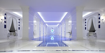 Un pasillo de hotel lujoso con suelo reflectante, columnas blancas y una piscina central.