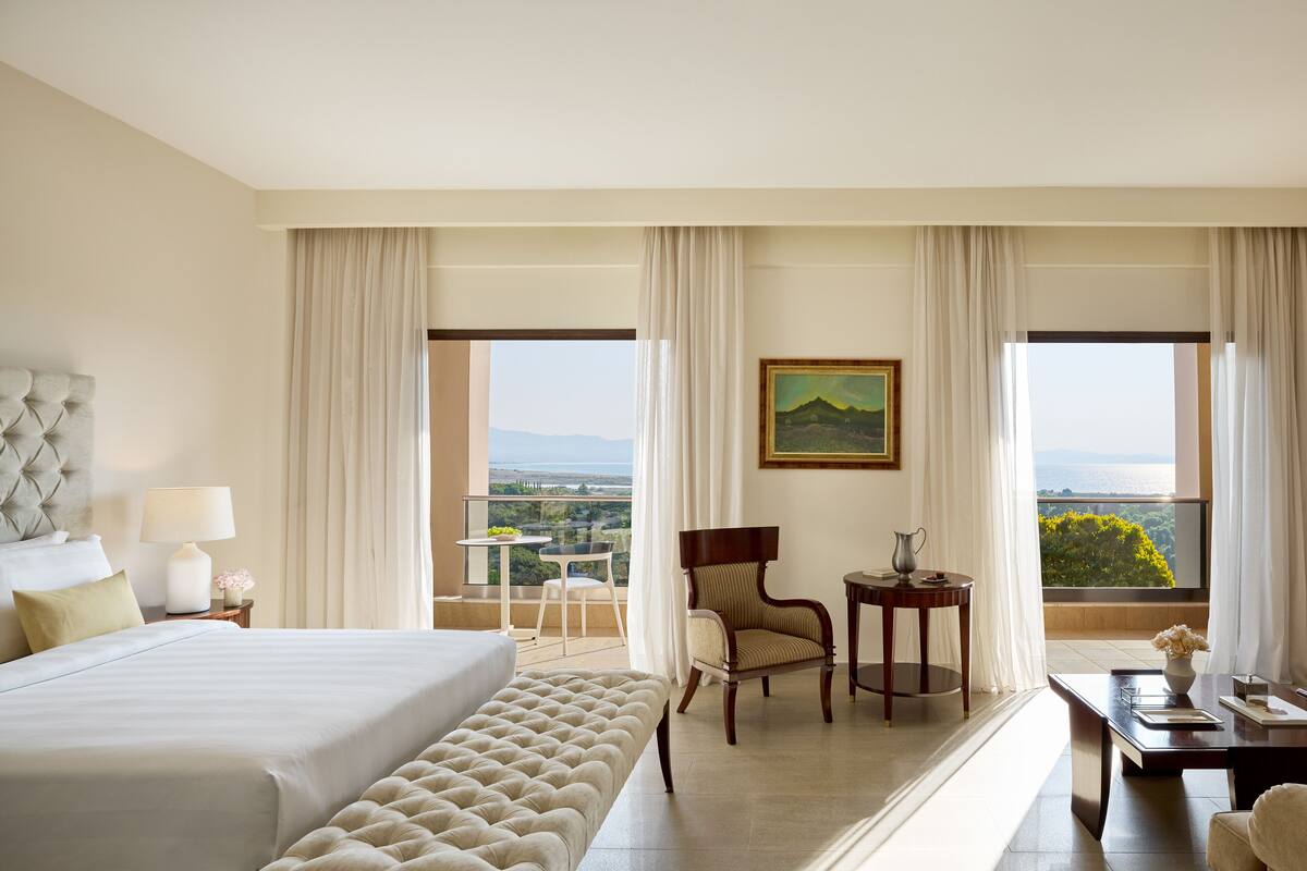 A hotel room with a large bed, a chair, a small table, and a view of the landscape.
