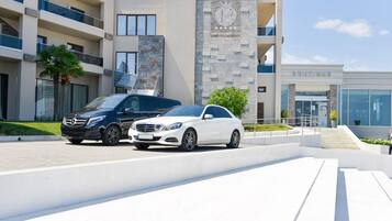 A modern wellness spa hotel with a prominent sign, a boutique, and two luxury cars parked in front.