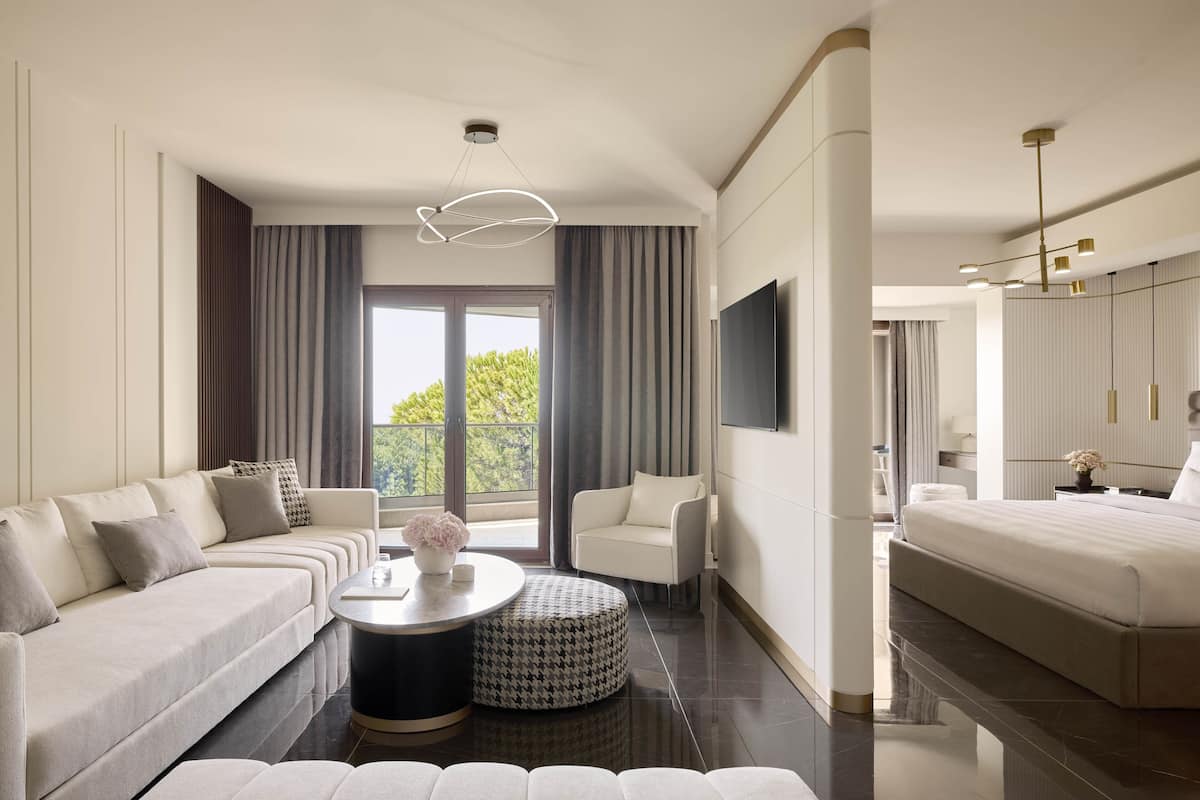 A modern hotel room with a sofa, a round coffee table, a chair, a bed, and a TV mounted on the wall.