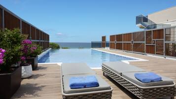 Un área junto a la piscina con sillones de descanso y vista al mar.