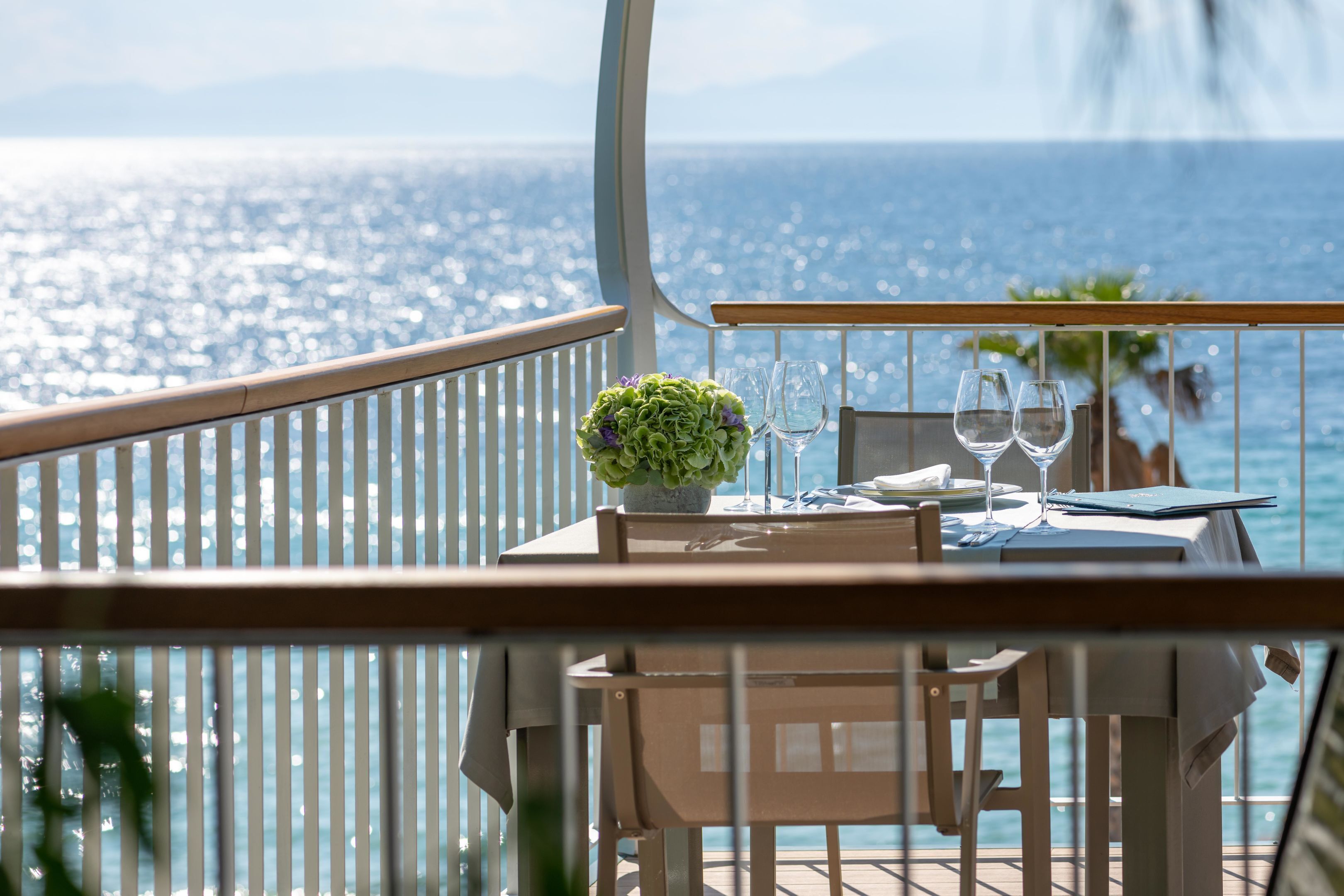 A dining table with two wine glasses and a menu, set against a scenic ocean view.