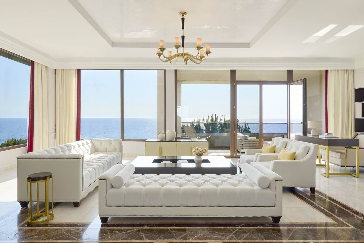 A spacious living room with a large sofa set, a coffee table, and a view of the sea.