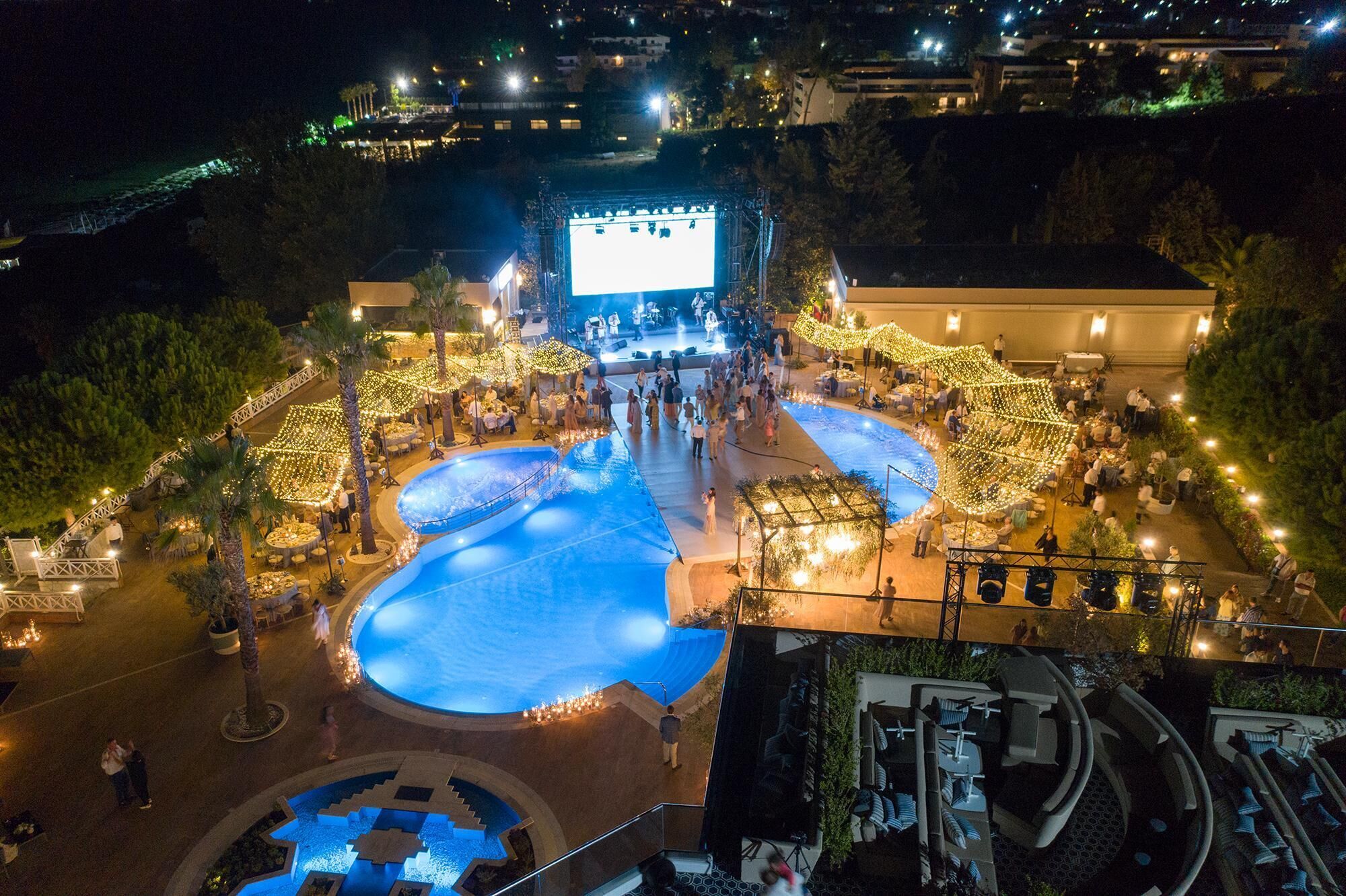 Ein Außenbereich mit einem zentral gelegenen Pool, Sitzbereichen und einer Bühne für Auftritte.