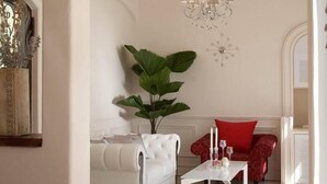 Ein geräumiges Wohnzimmer mit einem weißen Sofa, einem roten Sofa, einer großen Pflanze, einer Kristallleuchtre und einer Holzbalkendecke.