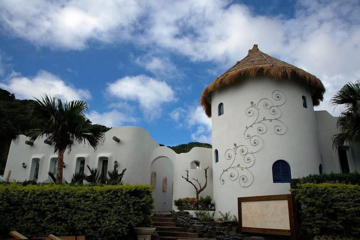 A white building with a thatched roof, surrounded by palm trees and a clear sky.