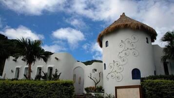 A white building with a thatched roof, surrounded by palm trees and a clear sky.