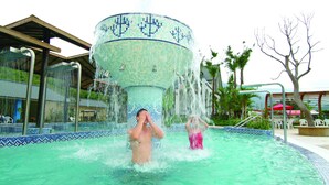 Ein Poolbereich mit einem zentralen Wasserspiel und umliegenden Liegestühlen.