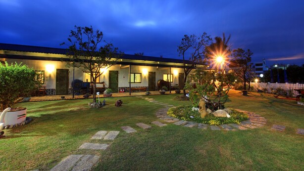 A well-lit residential building with a garden, stone pathway, and outdoor seating area.