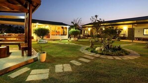 A well-lit outdoor area with a covered seating area, a small garden with a tree, and a building with multiple rooms.