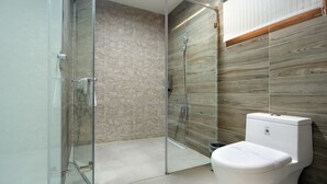 A modern bathroom with a glass shower enclosure, a white toilet, and a stone-textured wall.