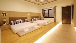 A hotel room with two beds, a wooden floor, a large window, and a door with a decorative panel.