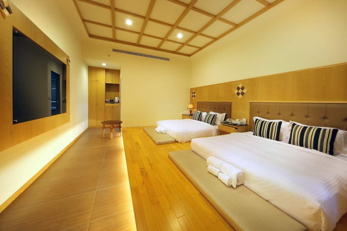 A hotel room with two beds, wooden flooring, a large mirror, and a wooden ceiling with a grid pattern.