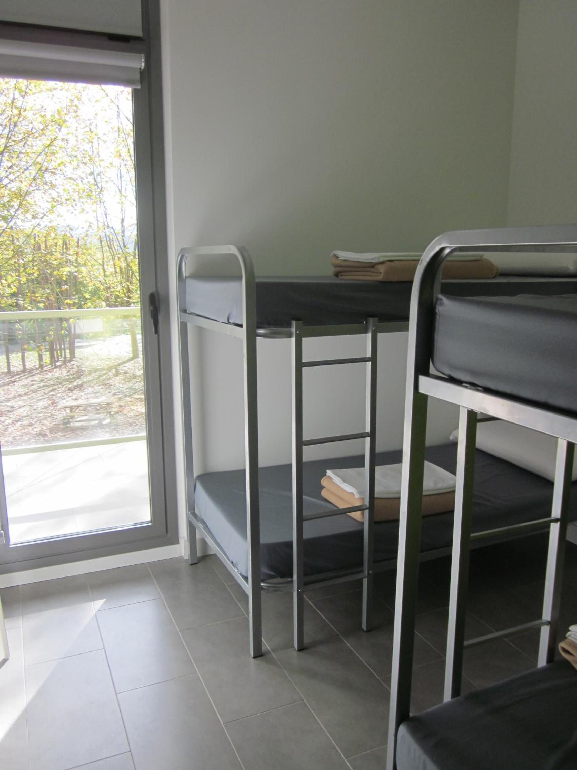 A dormitory room with bunk beds, a sliding glass door leading to an outdoor area, and a tiled floor.
