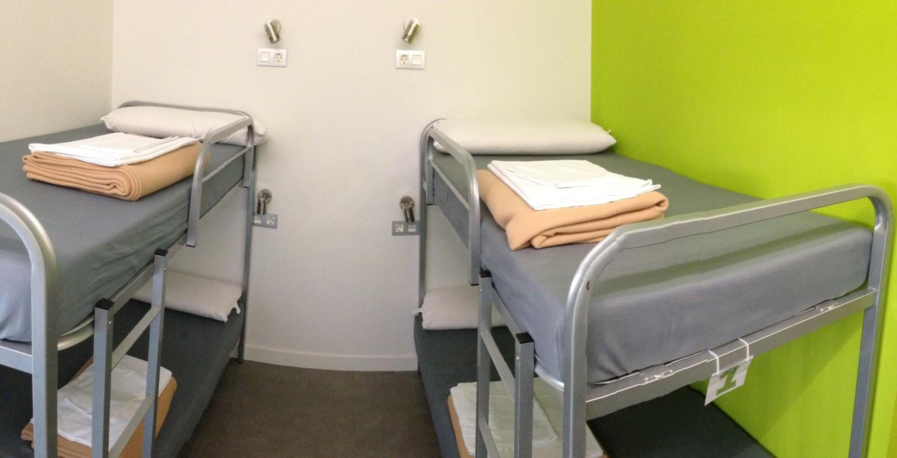 Two bunk beds with metal frames and grey bedding, a green wall, and a white door with electrical outlets.