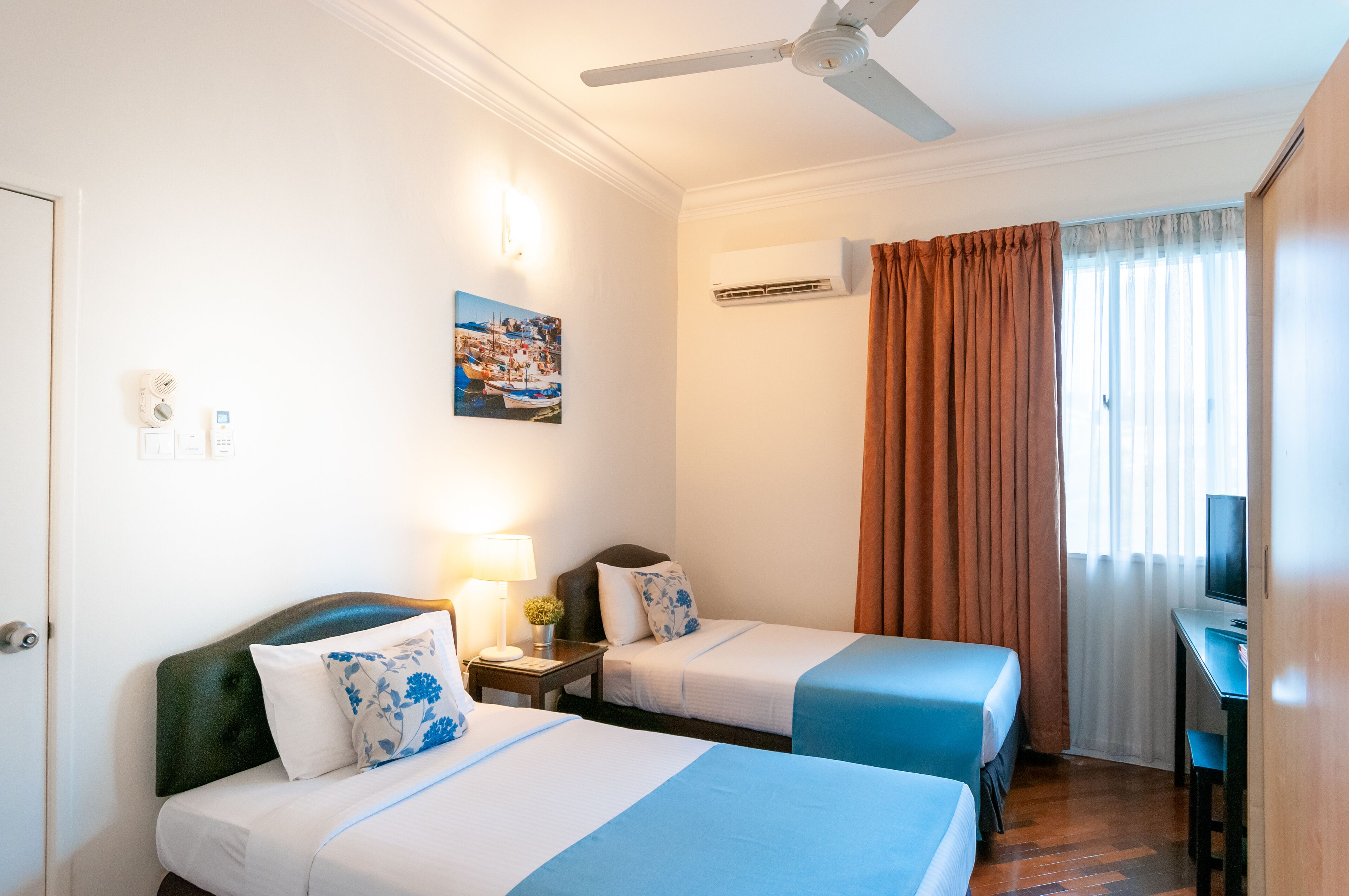 Een hotelkamer met twee bedden, een bureau, een televisie, een airconditioning en een schilderij aan de muur.