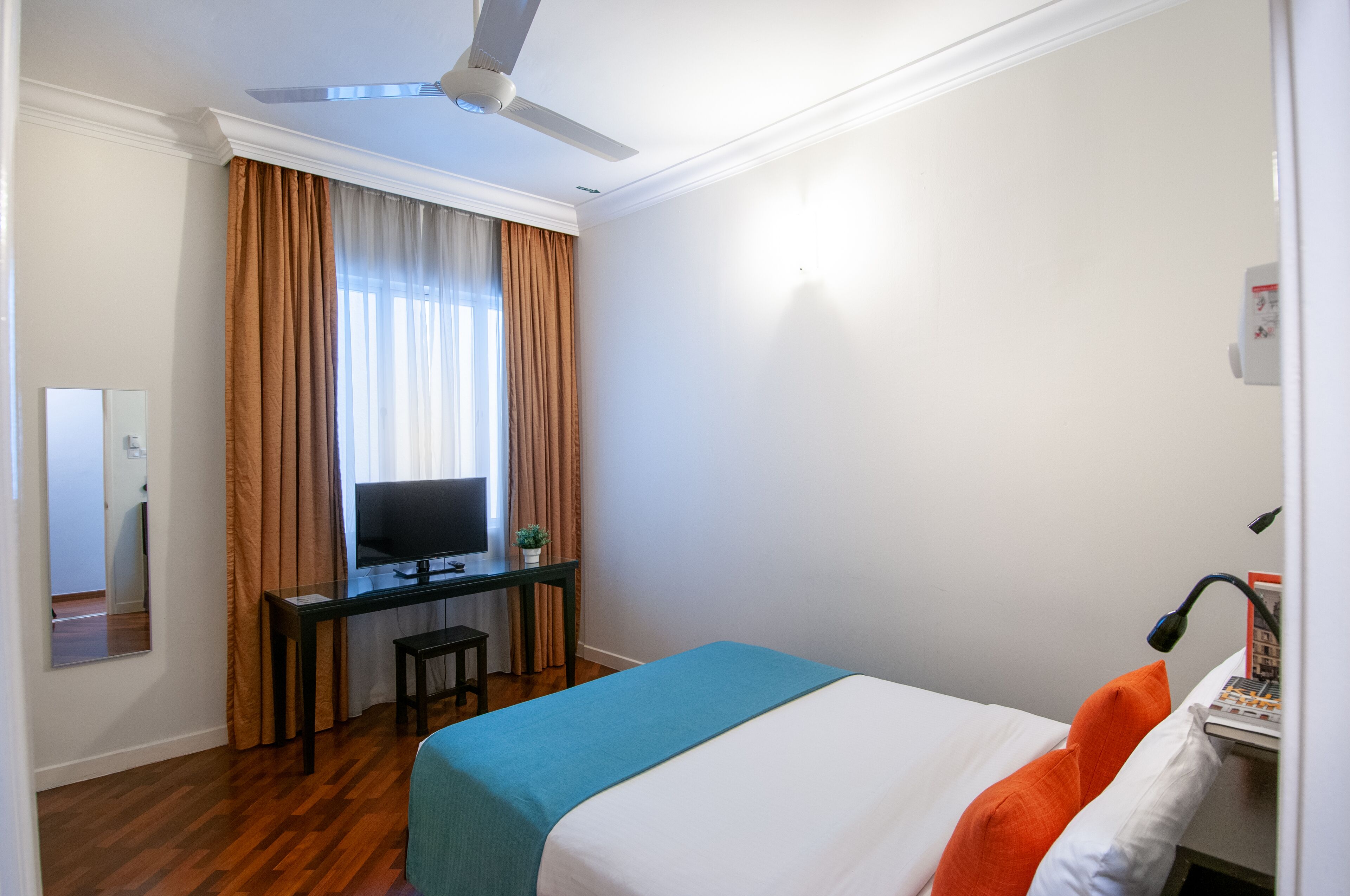 Una habitación de hotel con una cama, un escritorio con computadora, televisión y ventilador de techo.